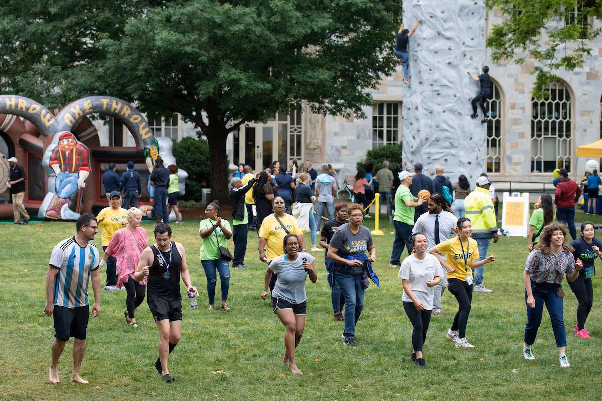 People participating in outdoor games at a community festival with a rock climbing wall and inflatable axe-throw attraction.
