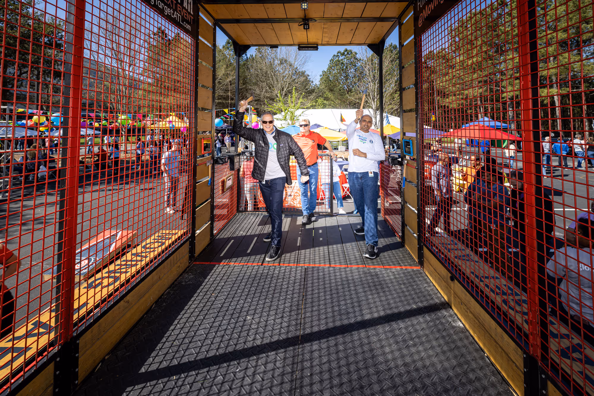 Event participants walking out of an axe-throw style booth at a community festival with tents and crowds in the background.