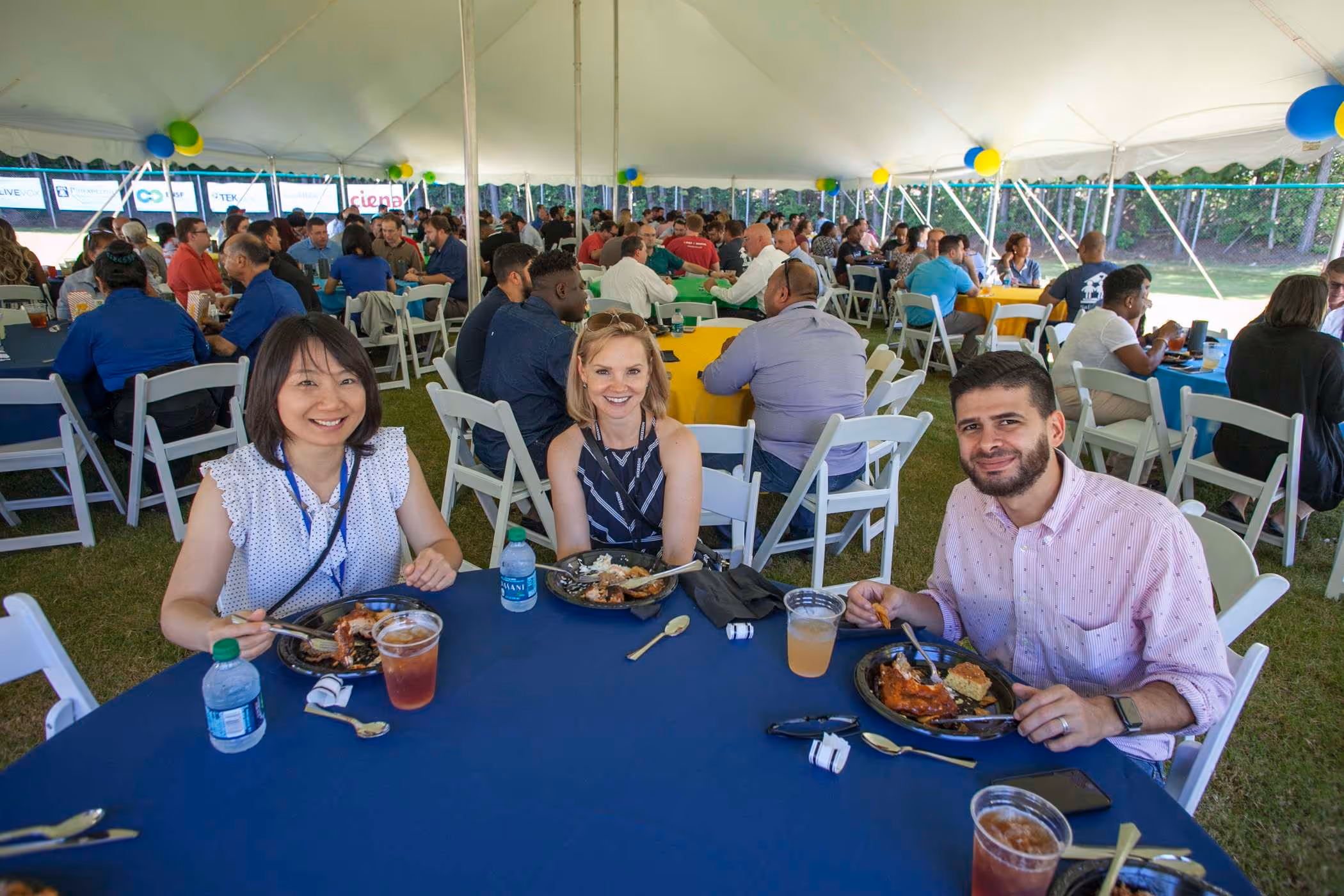 Employees enjoying lunch together under a large outdoor event tent during a corporate gathering.