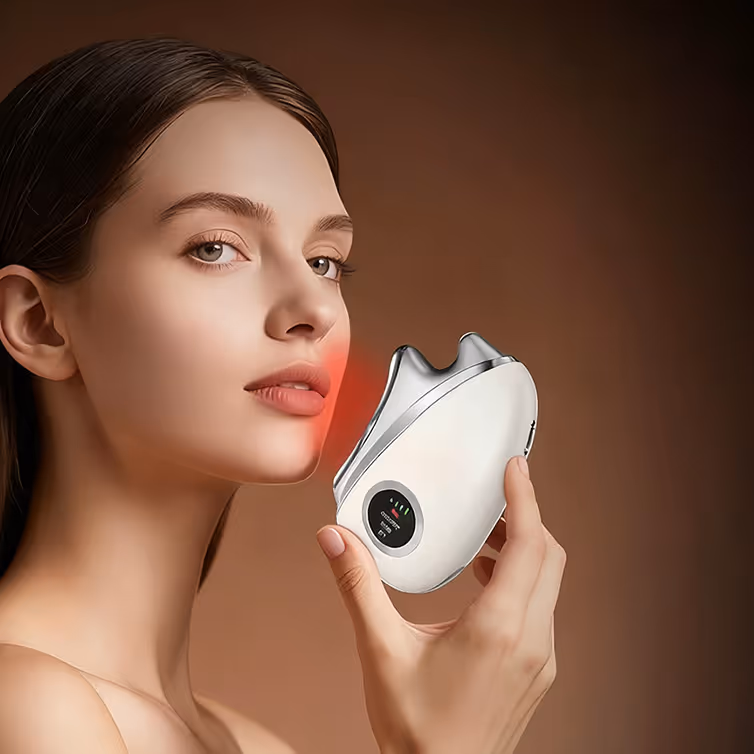Woman using a white handheld facial device emitting red light on her cheek against a brown background.