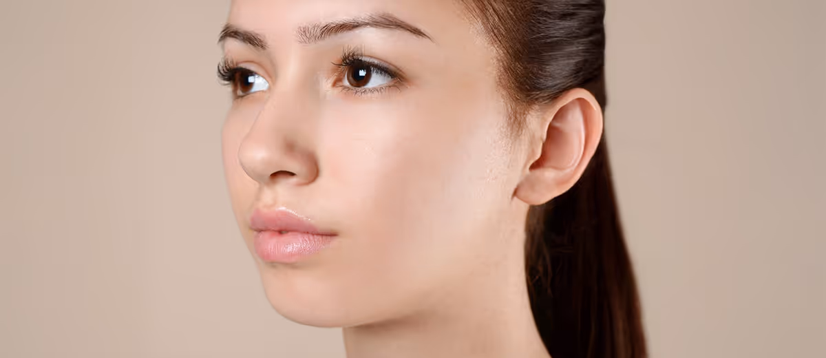 Close-up of a young woman with clear skin, looking slightly to the left against a beige background.