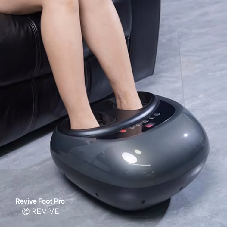 Person using a sleek black foot massager on a gray floor beside a black leather couch.