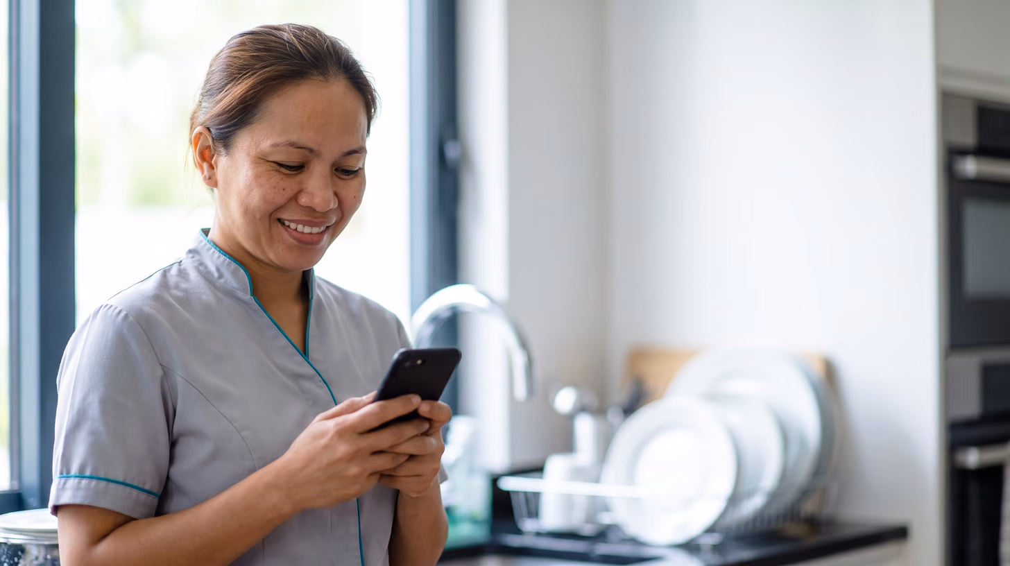 Housekeeper smiling at her phone after sending photo proof of washed plates from a housekeeping app