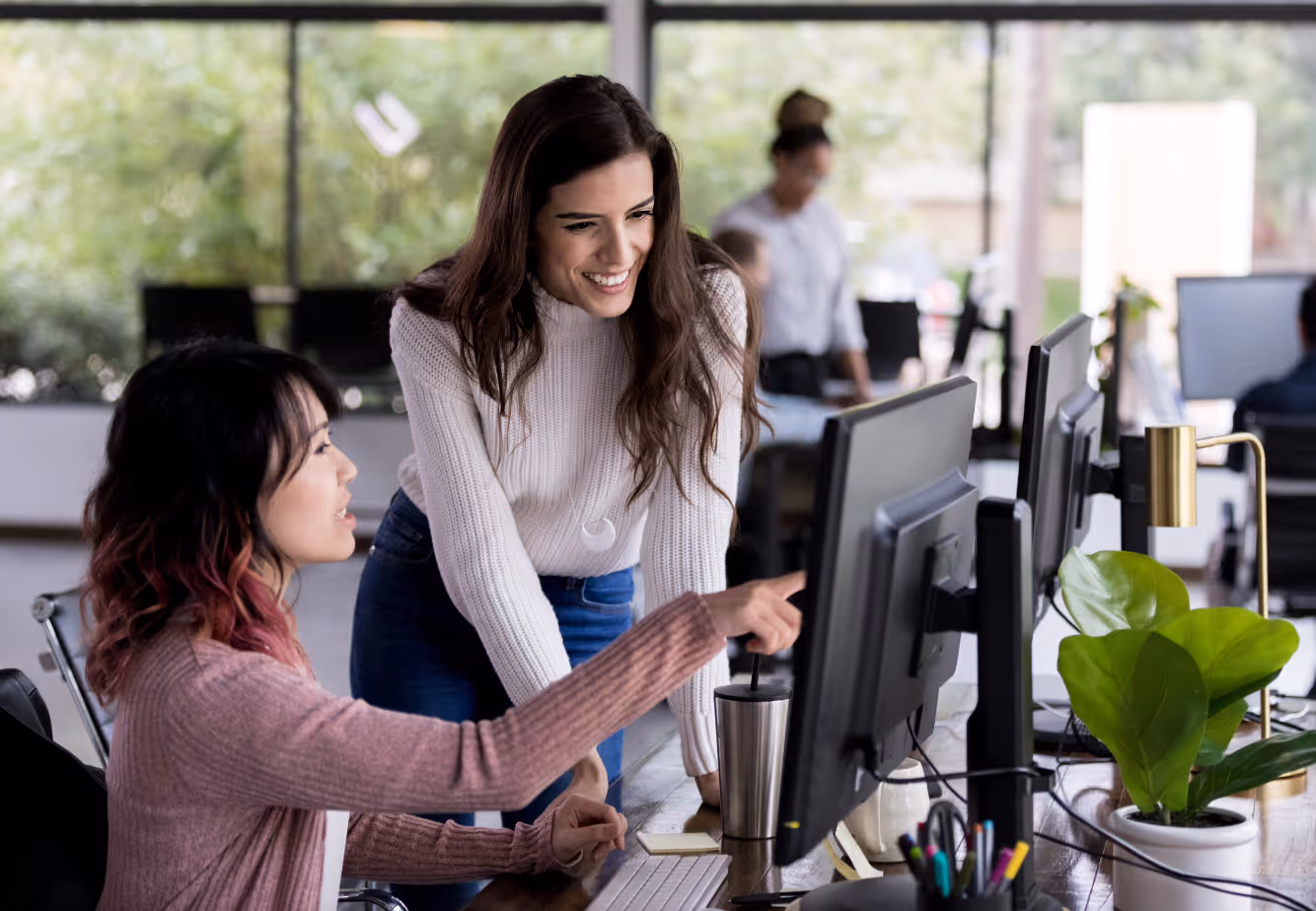 Two people looking at the same computer. One is pointing to the screen. The other is smiling.