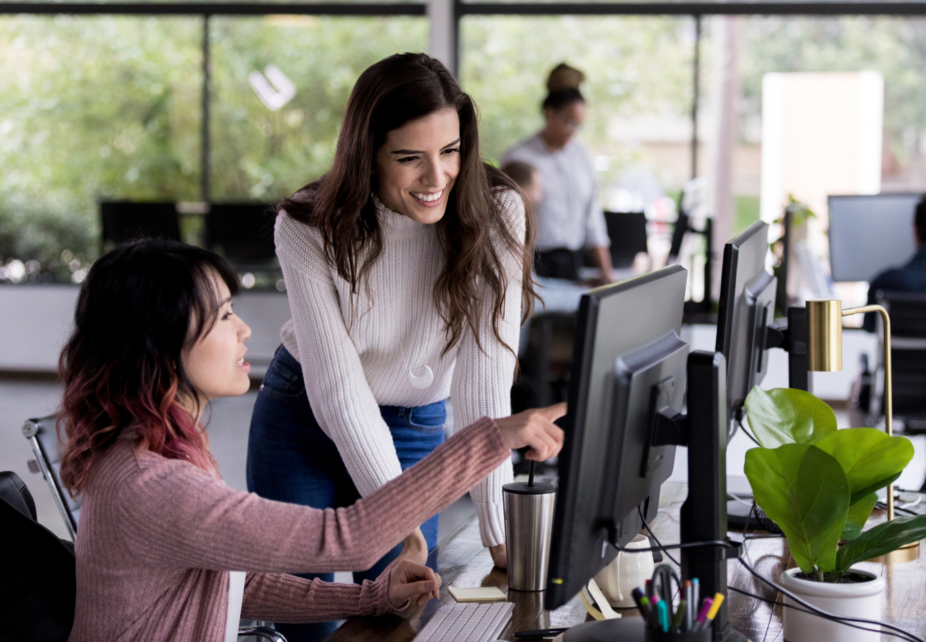 Two people looking at the same computer. One is pointing to the screen. The other is smiling.