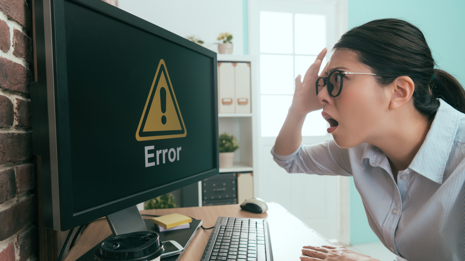 Women with a hand on her head and shocked face looking at a computer screen with an error message. Looking in distress.