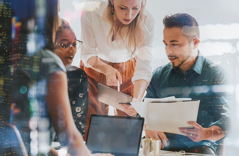 Group of three people looking at information on a tablet. One man holds a folder with papers in it.