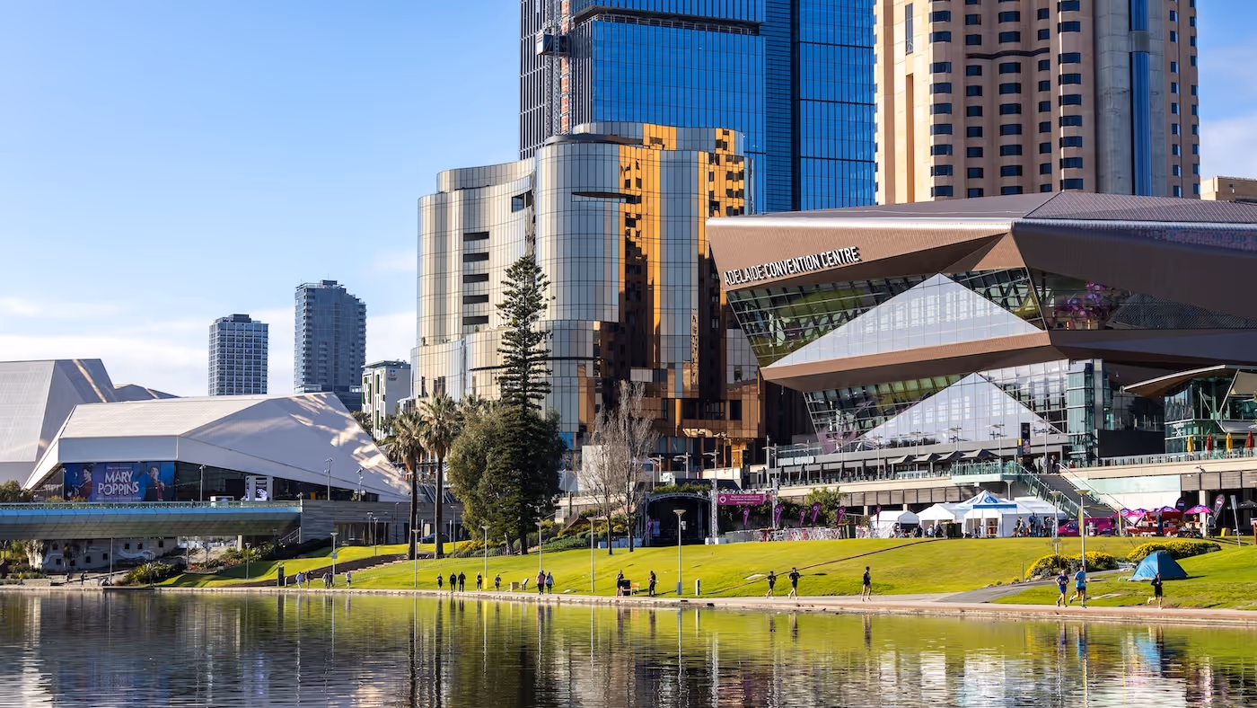 Adelaide Convention Centre and city skyline reflected in River Torrens with people walking along the riverbank.