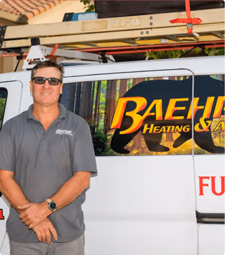 Man wearing sunglasses and gray polo shirt standing with hands clasped in front of a white van with Baehr Heating & Air logo and a ladder on top.