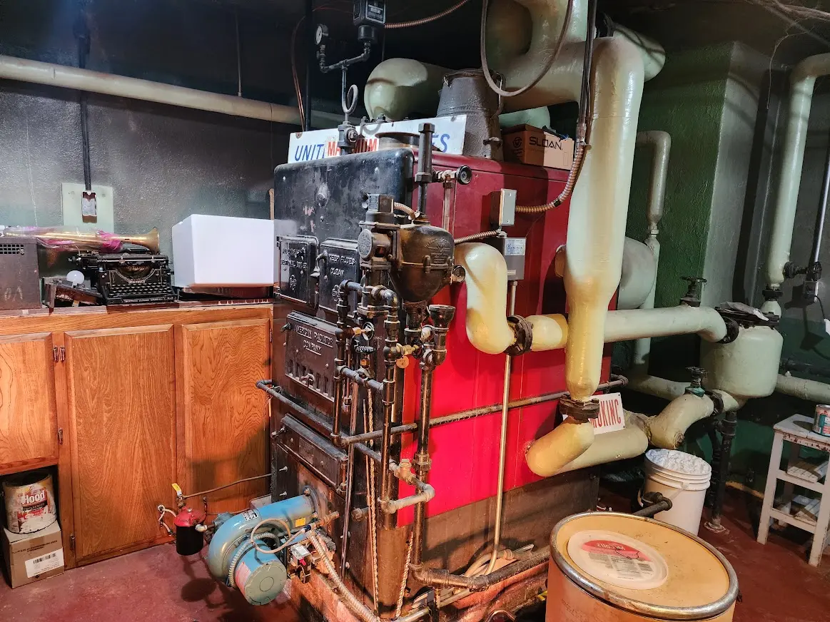 Industrial boiler with yellow insulated pipes in a maintenance room with wooden cabinets and cleaning supplies.