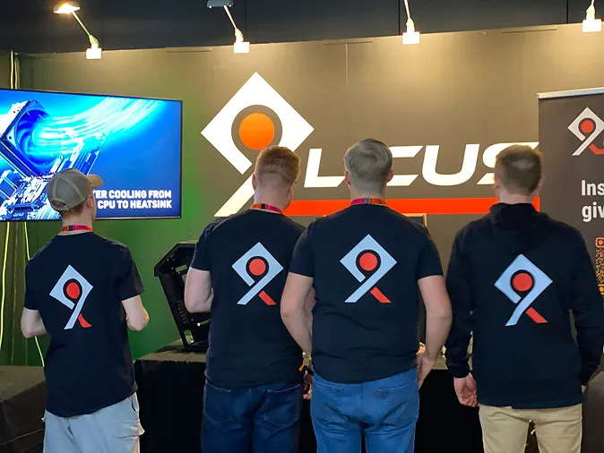 Four men standing with their backs to the camera wearing black shirts and a hoodie with a logo featuring a white diamond shape, a red circle, and an orange angled line.