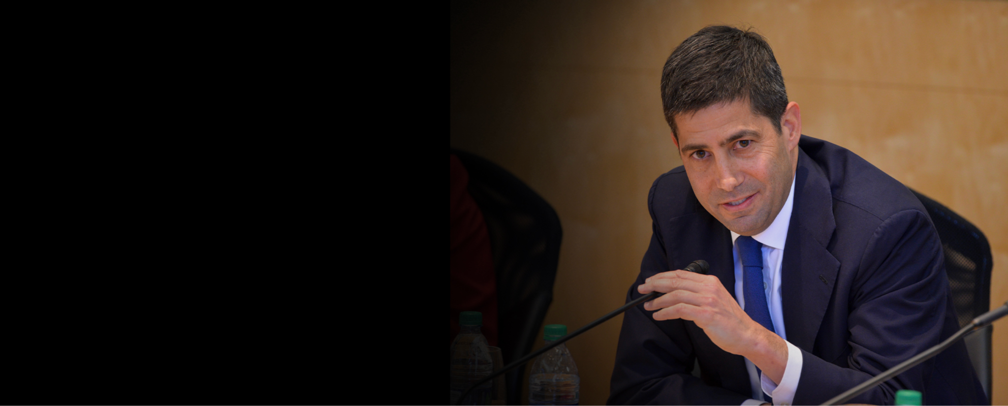 Kevin Warsh at a policy hearing, leaning forward at the table — confirmed as 17th Fed Chair in May 2026