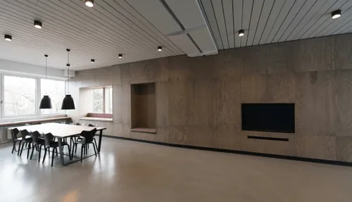 Modern conference room with large wooden table, black chairs, pendant lights, and wall-mounted TV.