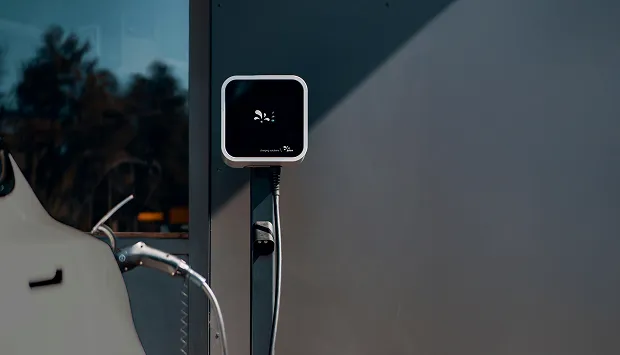 Close-up of an electric vehicle charging station mounted on a dark wall with a charging cable connected to a white vehicle.