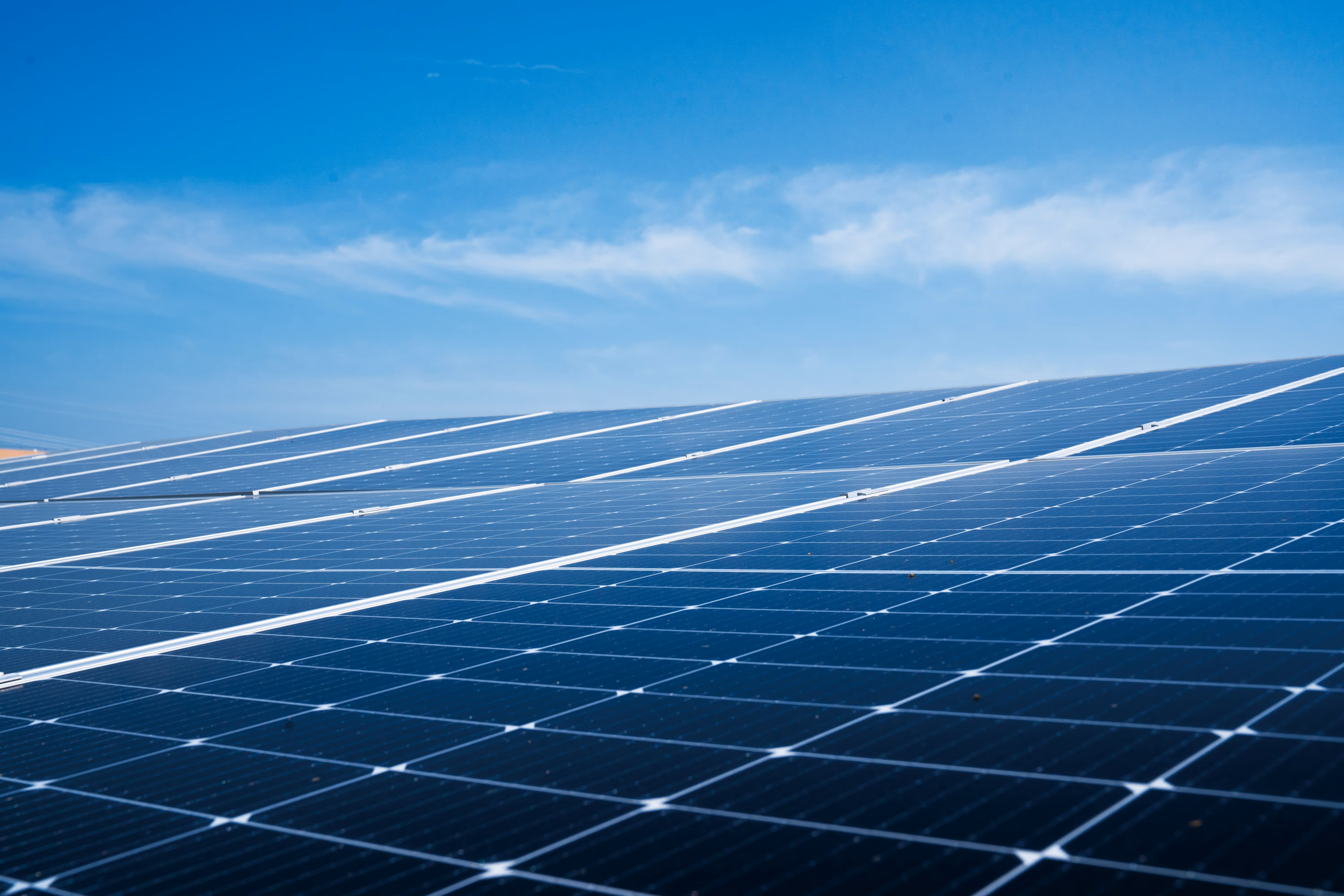 Rows of solar panels under a clear blue sky with scattered clouds.