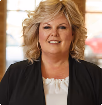 Smiling middle-aged woman with curly blonde hair wearing a black blazer and white blouse.