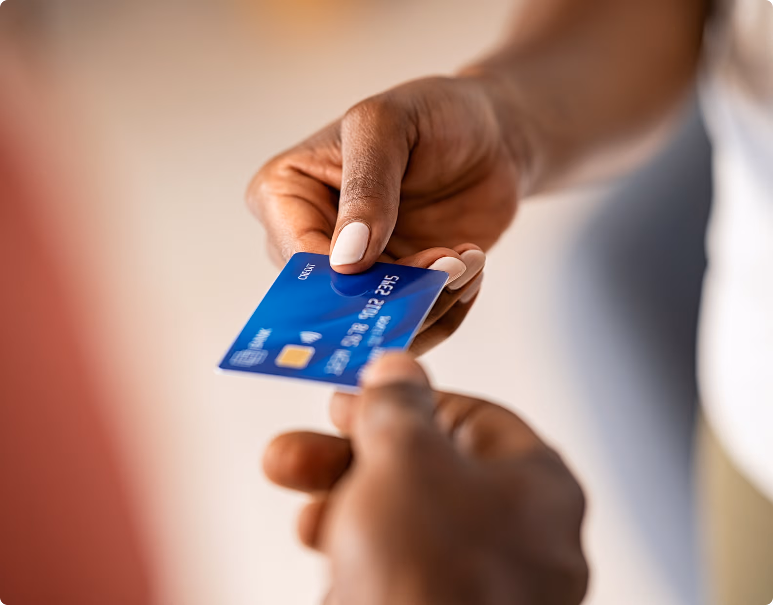 Close-up of a person handing a blue credit card to another person.