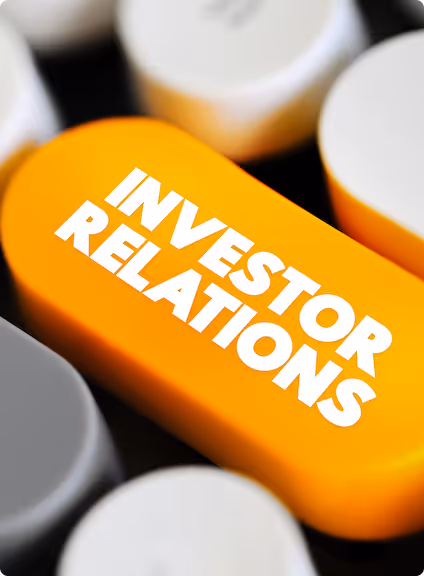 Close-up of an orange pill-shaped object with the words 'INVESTOR RELATIONS' in bold white letters surrounded by blurred white and gray circular shapes.