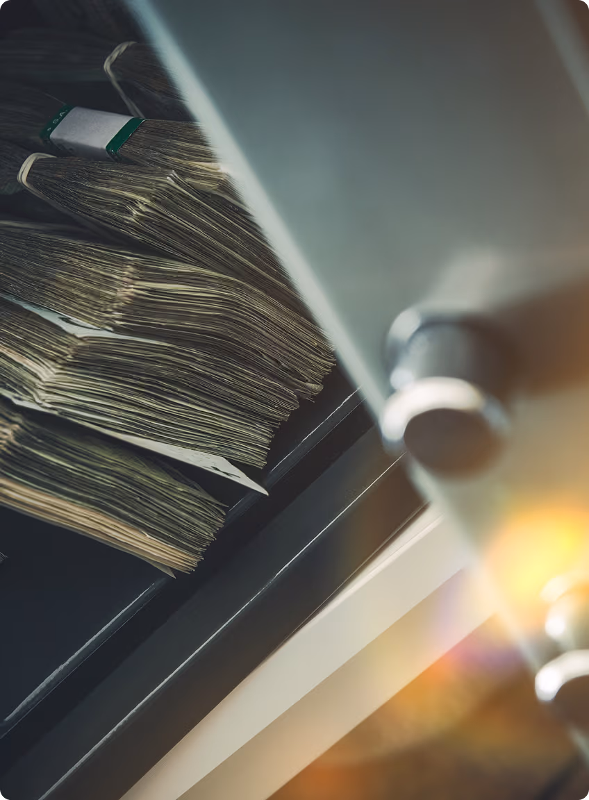 Stacks of bundled cash visible inside a partially open safe with light reflections.