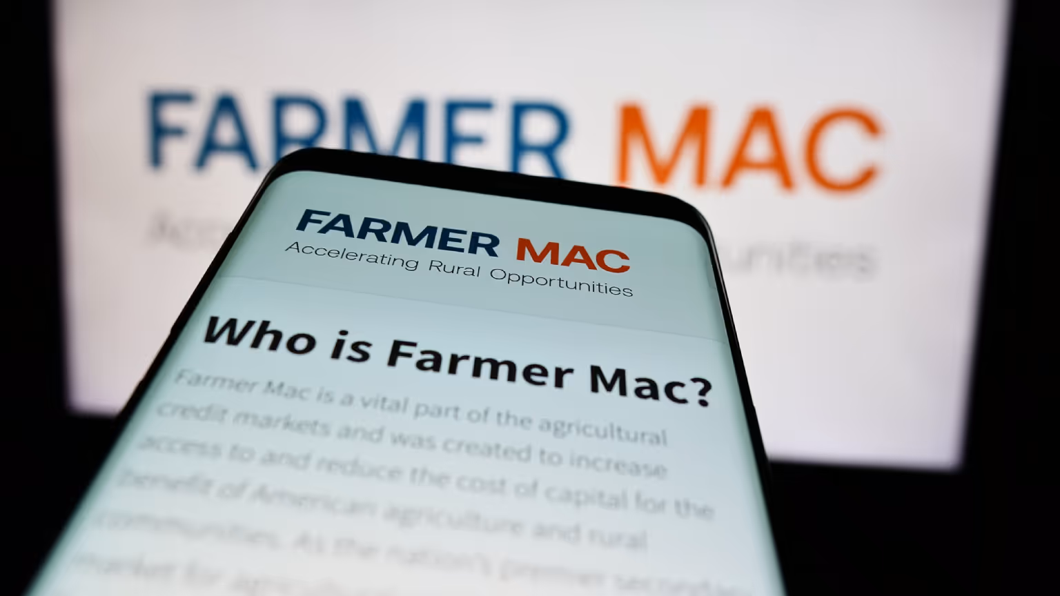 Smartphone screen showing 'Who is Farmer Mac?' with Farmer Mac logo and slogan 'Accelerating Rural Opportunities' blurred background.