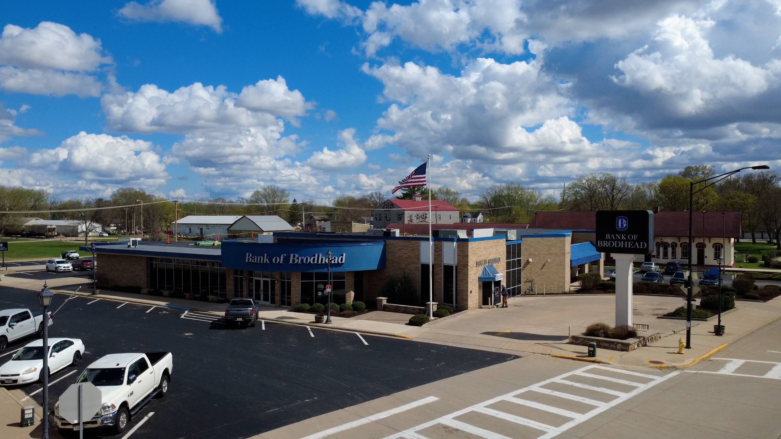 Aerial view of Bank of Brodhead building with parked cars and an American flag in front.