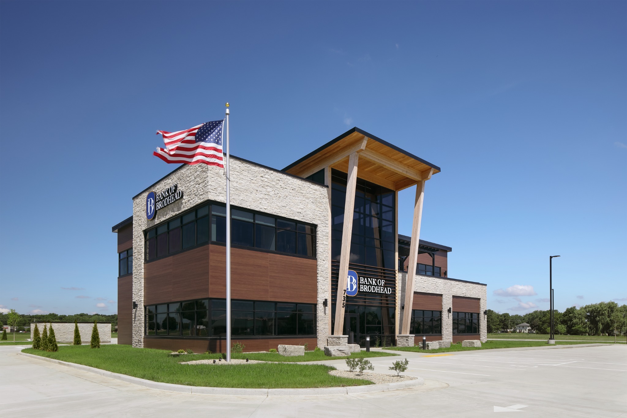 Modern two-story Bank of Brodhead building with stone and wood paneling and an American flag.