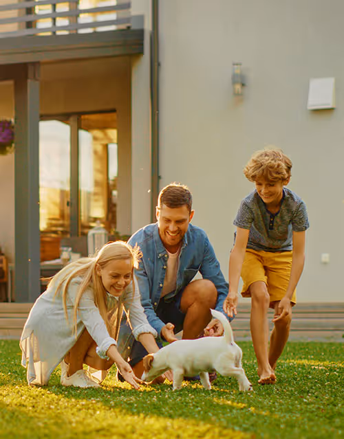 young family playing happily with small dog on lawn