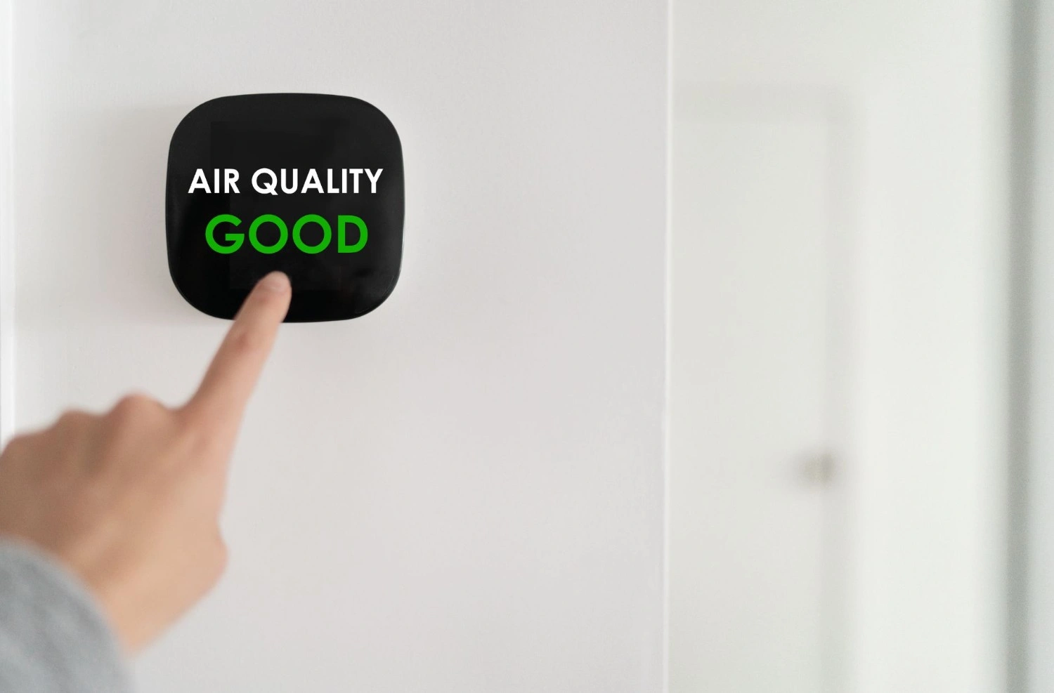 Hand pointing to air quality monitor.