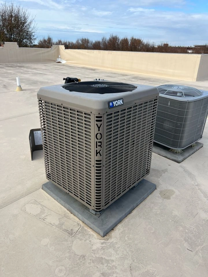 Two York air conditioning units are on a flat rooftop under a blue sky. 
