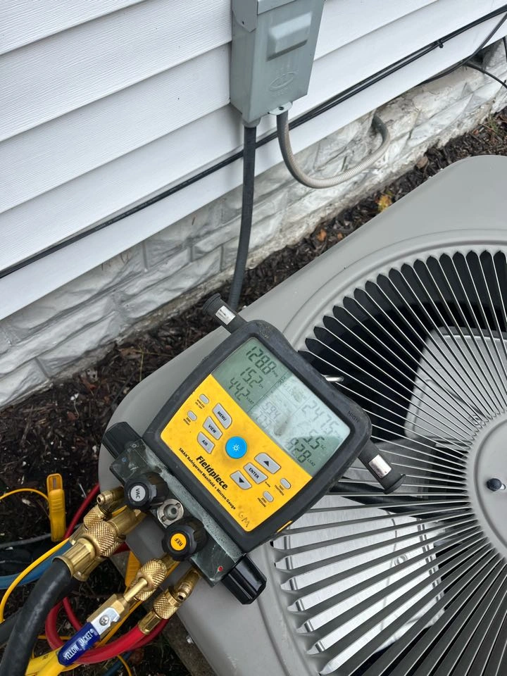 A digital HVAC gauge resting on a gray outdoor air conditioning unit, displaying various readings. 