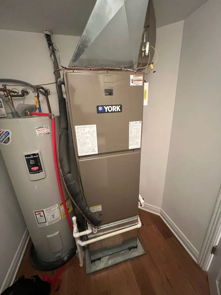York furnace and water heater in a small utility room with white walls and wood flooring. 