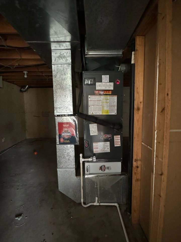 Metal furnace system in a dim basement, with exposed ducts and labeled panels.
