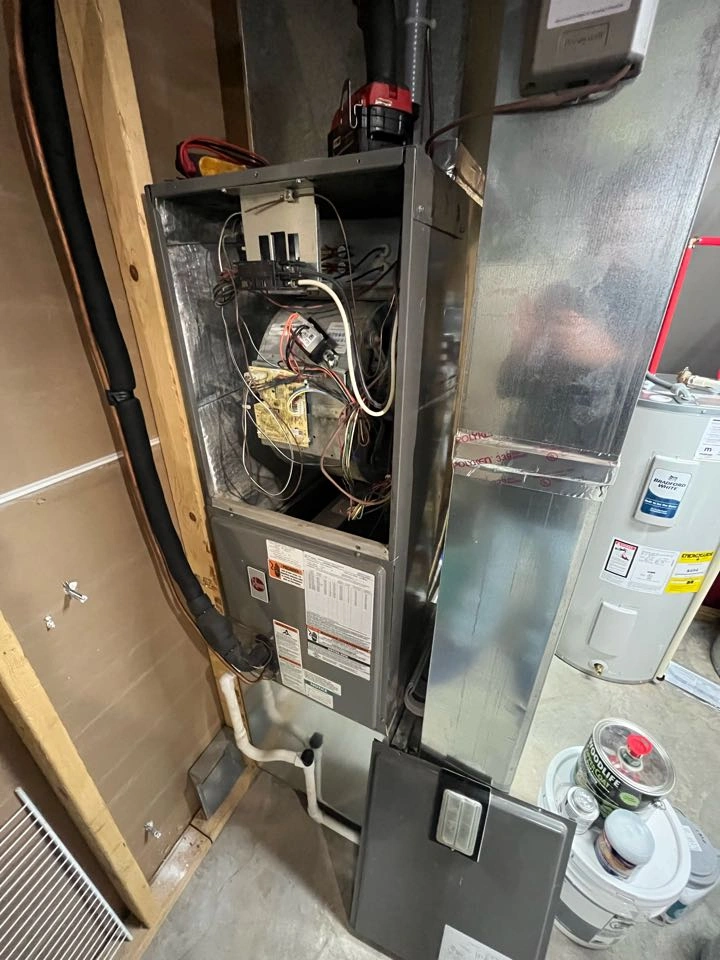 Open furnace showing inner wiring and components, in a basement setting.