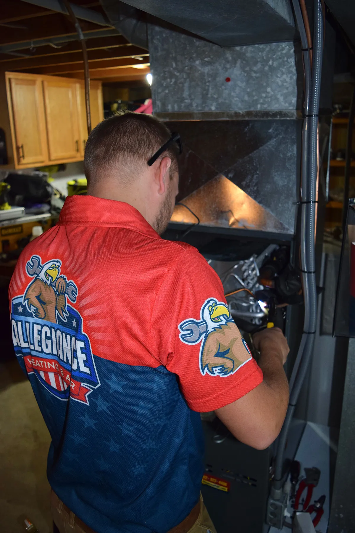 Technician in Allegiance Heating & Air uniform servicing a furnace in a residential setting, highlighting HVAC maintenance and installation expertise.