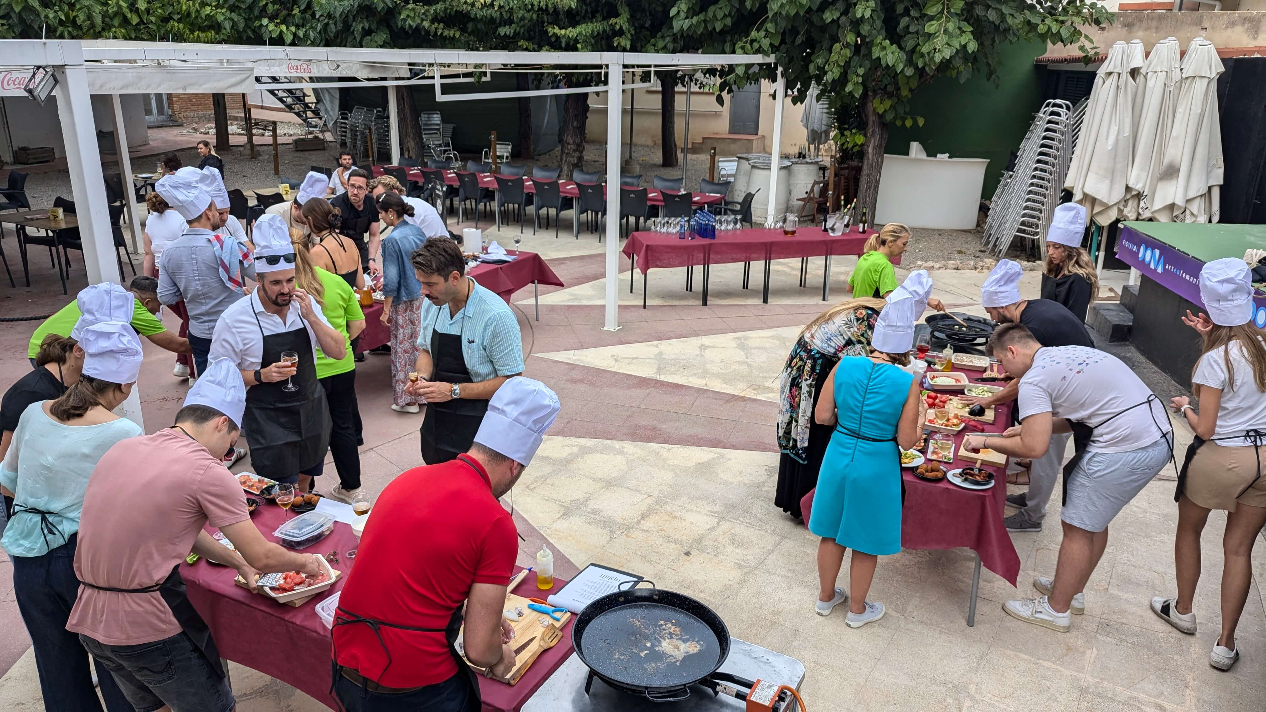 Outdoor cooking class with participants wearing chef hats and aprons preparing food around tables.