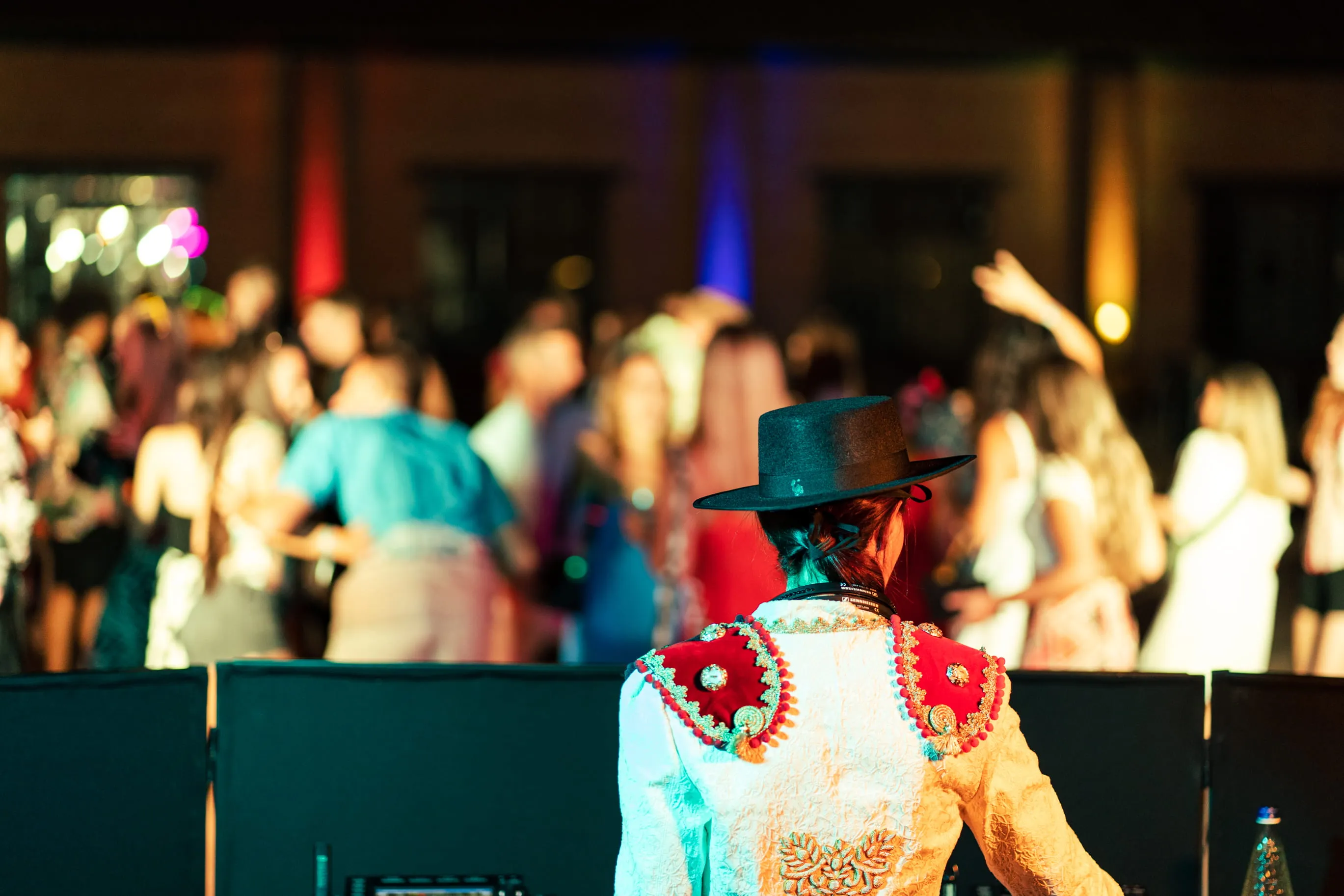 Person in traditional matador costume and black hat facing a blurred crowd at an indoor event.