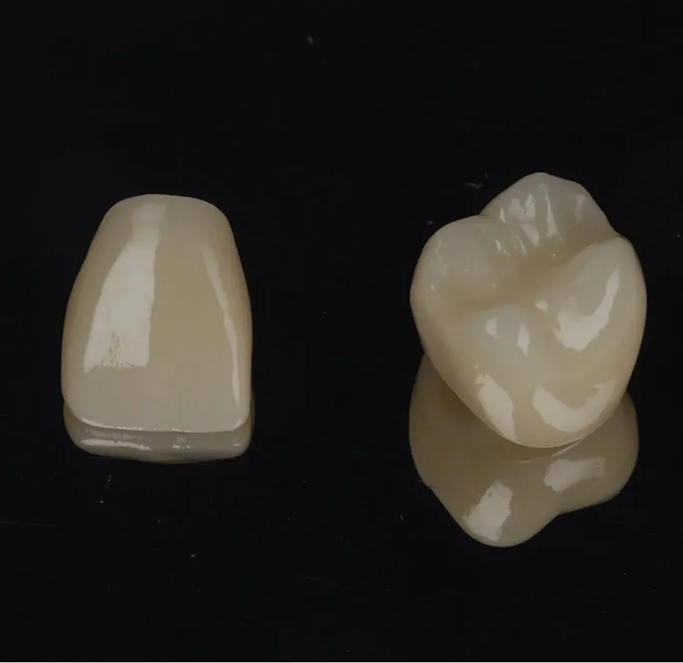 Two dental crowns, one shaped like a front tooth and the other like a molar, on a reflective black surface.
