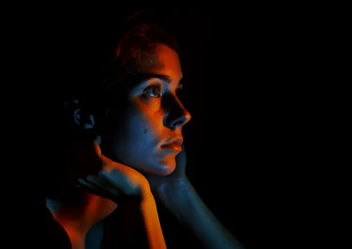 Portrait of a woman illuminated by contrasting blue and orange lighting against a dark background.