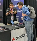 Two men interacting at a Cloaked exhibition booth with a laptop on the table.