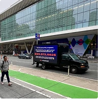 Black truck with advertisement for Security Expert parked beside a building with glass facade and green bike lane in front.