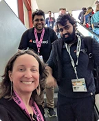 Three people wearing conference badges smiling and posing for a photo on a staircase.