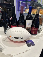 White football with 'cloaked' logo in front of five varied wine bottles on a marble countertop.