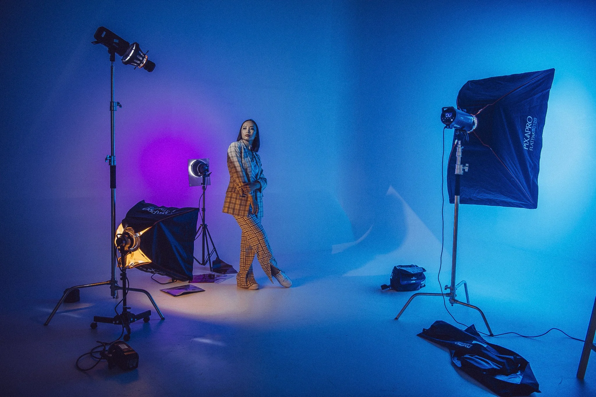 Kvinde i ternet jakkesæt poser foran farvet lys i et fotostudie med professionelt lysudstyr.