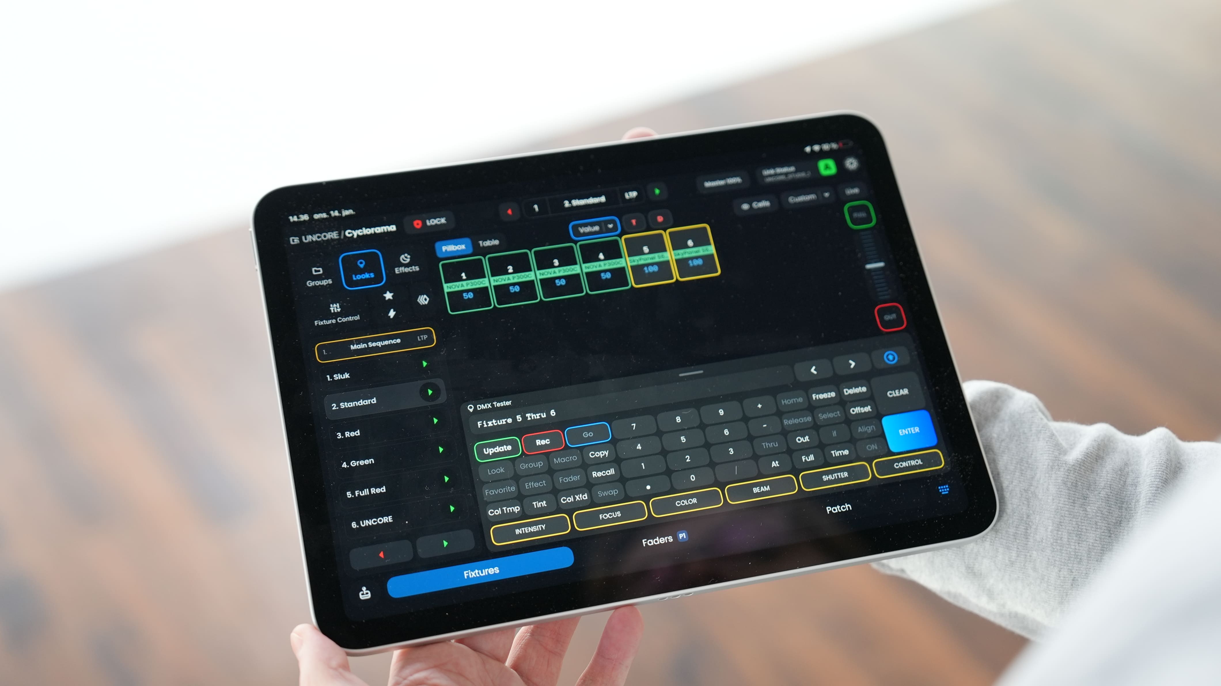 En person holder en tablet, der viser et kontrolpanel med lysindstillinger og knapper til DMX-lyssoftware.