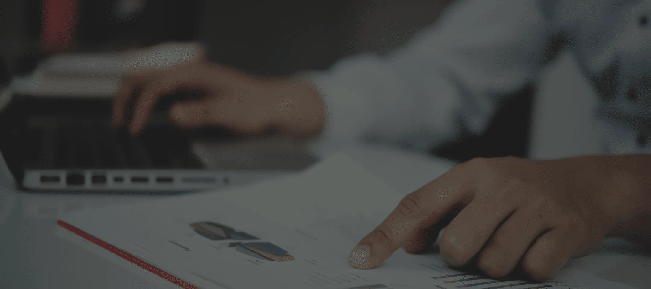 Una mano che indica un grafico su un documento mentre l'altra mano digita sulla tastiera di un laptop.