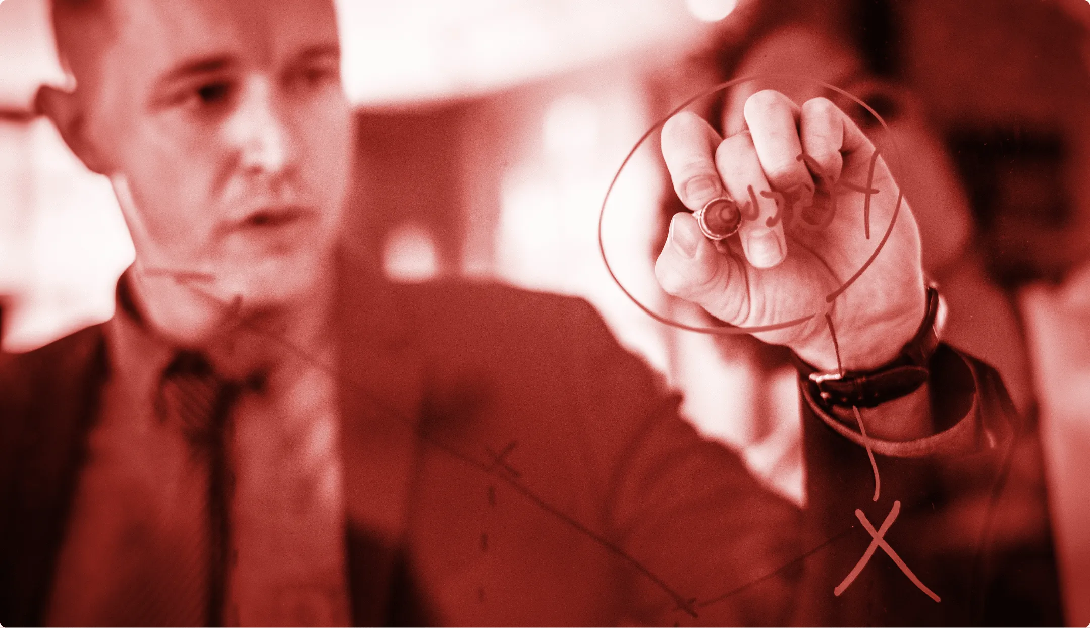 Un uomo in giacca e cravatta scrive strategie o diagrammi su una lavagna di vetro.