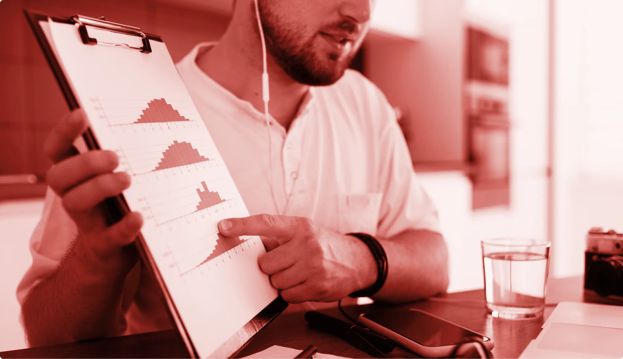 Uomo con auricolari che mostra grafici a barre su un blocco note in un ambiente da ufficio.