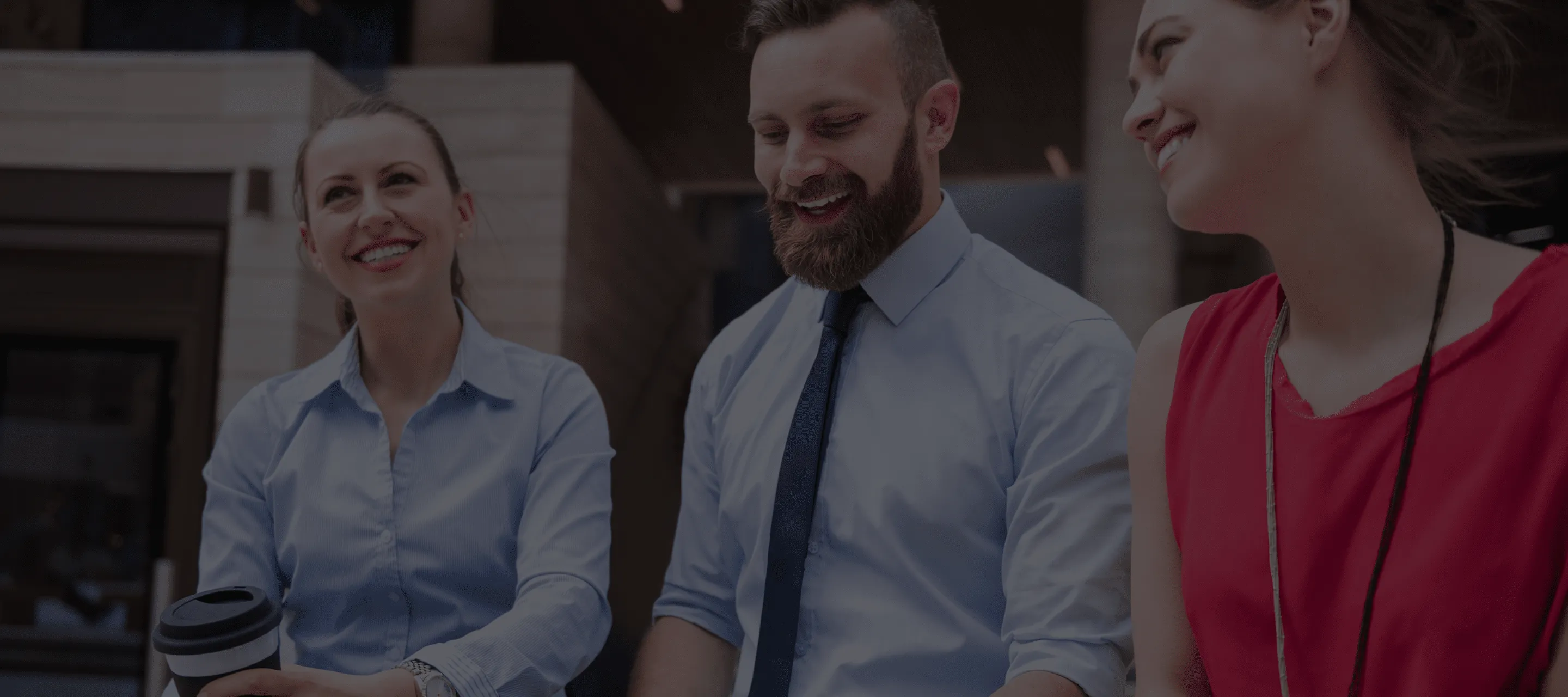 Tre persone sorridenti in abbigliamento professionale stanno parlando e interagendo insieme in un ambiente lavorativo.