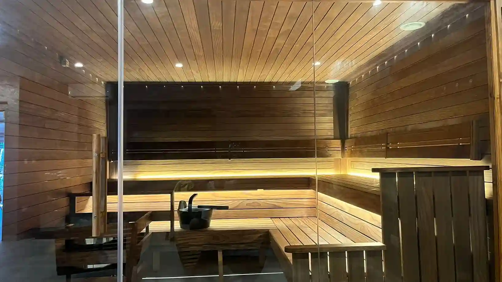 Interior of a modern wooden sauna room with bench seating and warm ambient lighting.