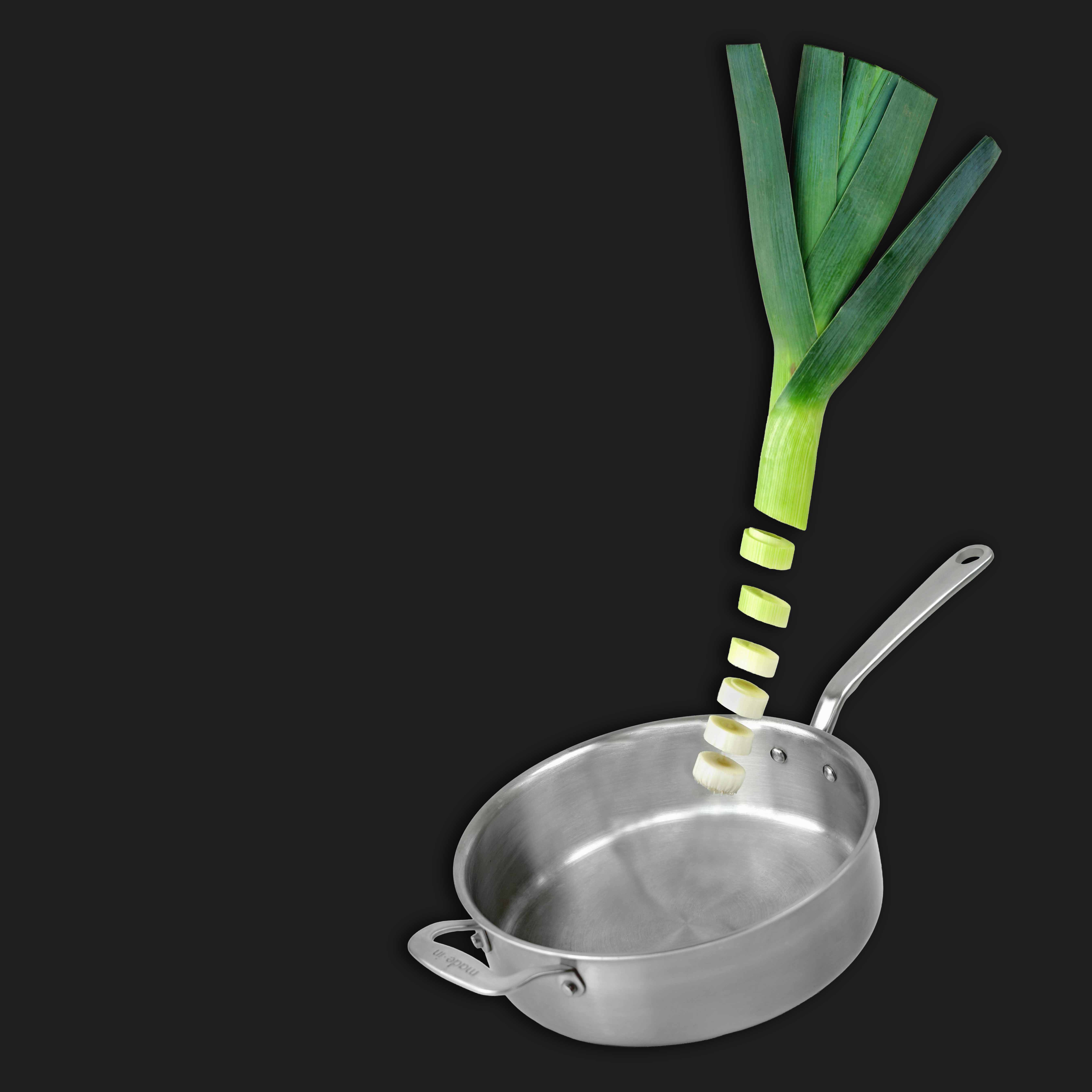 Frisch geschnittene Lauchscheiben fallen in eine leere Edelstahpfanne vor schwarzem Hintergrund.